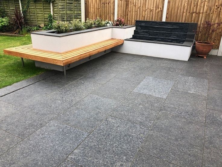Grå terrassefliser i natursten ved en plantebænk og siddeplads